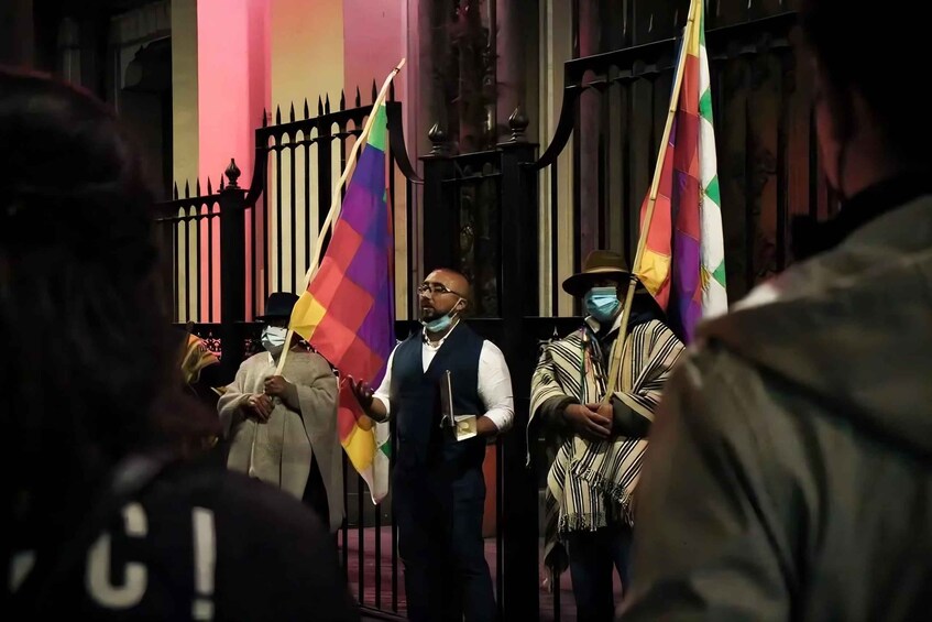 A group of people holding flags in front of a building with a black iron fence. 5