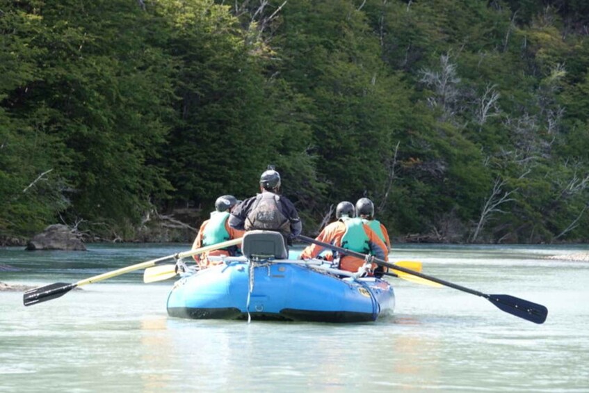 A group of people in a blue raft on a river surrounded by dense forest. 3