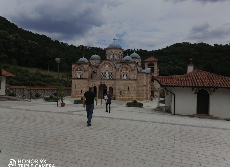 A historic church with multiple domes and crosses, surrounded by a paved courtyard and a hillside. 1
