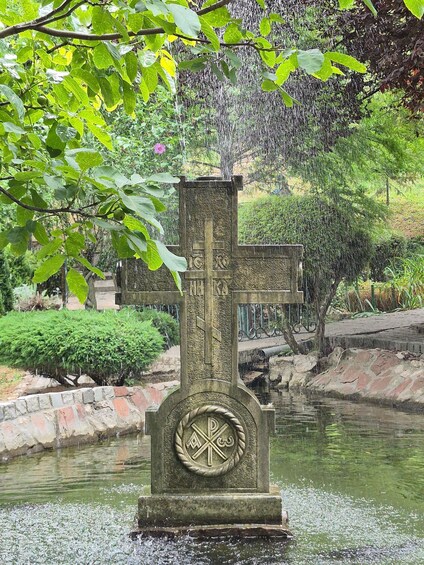 A stone cross with inscriptions in a park with a pond and greenery. 4