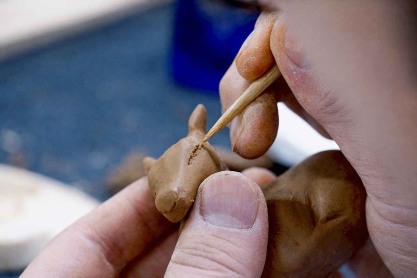 A person sculpting a clay figure with a tool. 2