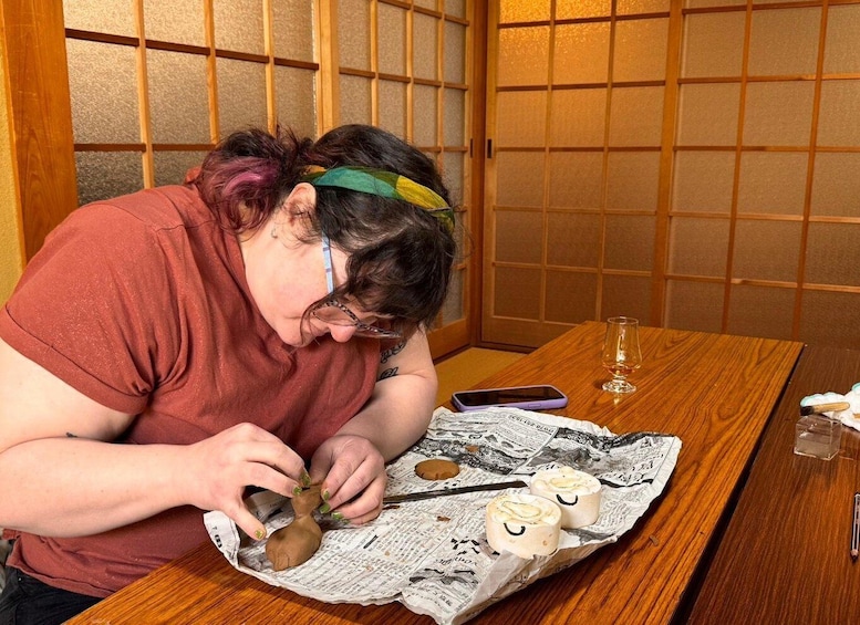 A person sitting at a wooden table, working on a craft project with clay on newspaper. 4