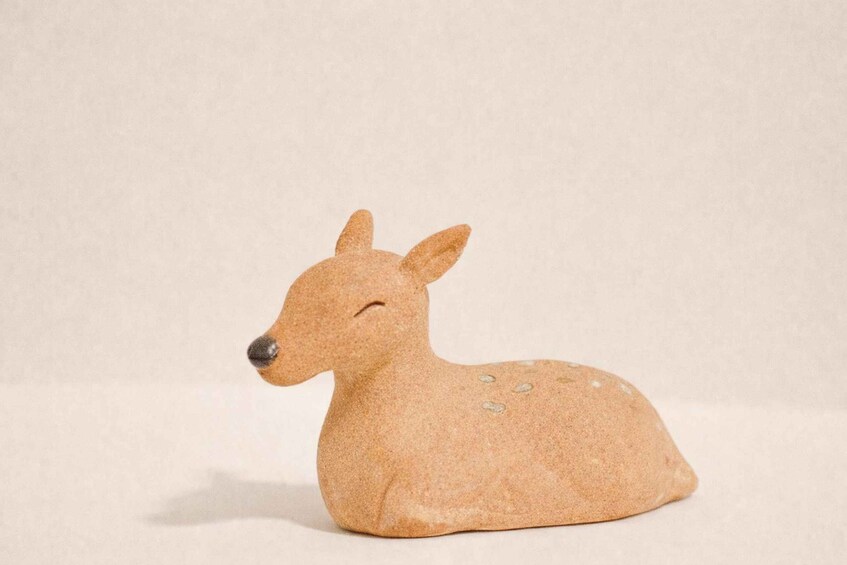 A small, light brown ceramic deer figurine with a dark nose and two antlers, lying on its side. 3