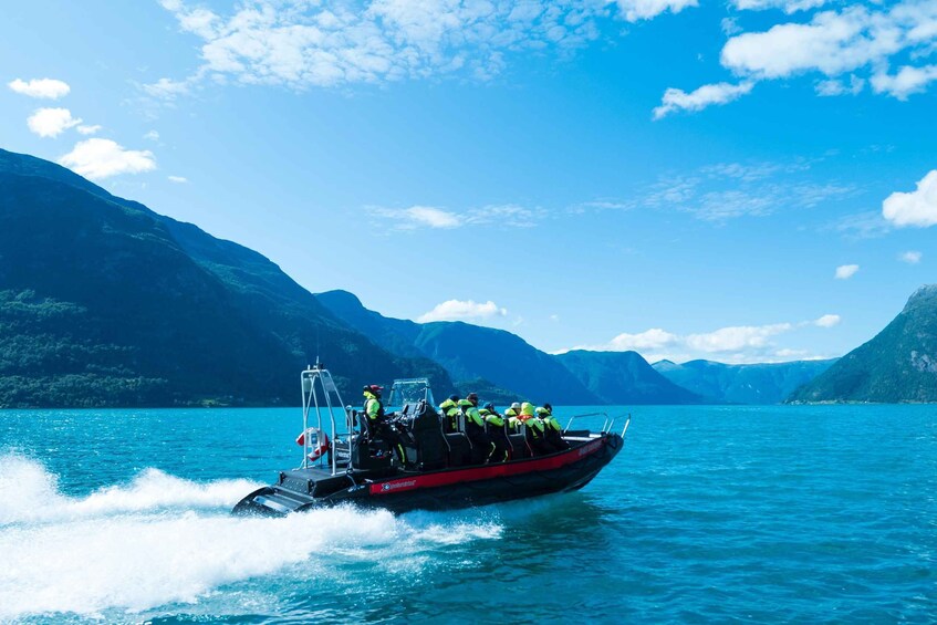 A speedboat with passengers wearing life jackets on a calm lake surrounded by mountains. 1