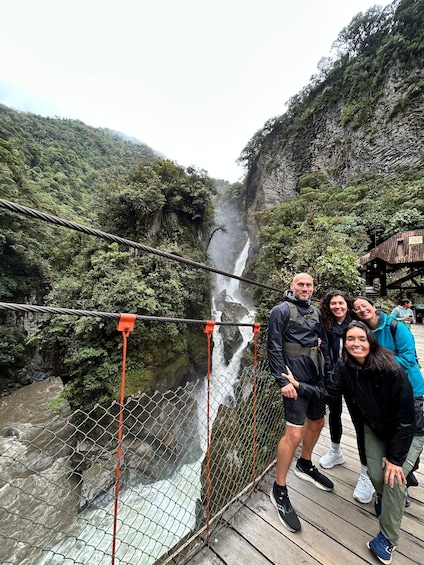 A group of people on a suspension bridge over a waterfall with lush greenery in the background. 2