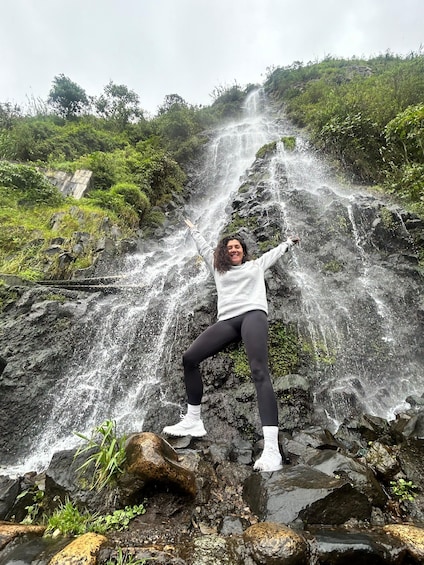 A person posing in front of a waterfall with arms raised. 5