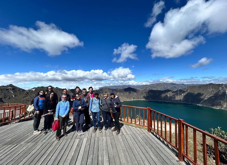 A group of people on a wooden deck overlooking a lake with mountains in the background. 1