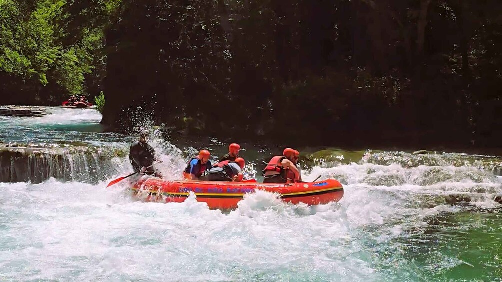 A group of people in a red raft navigating through a river with rapids. 5