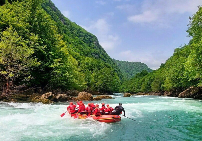 A group of people in a red raft navigating a river surrounded by lush green hills. 3