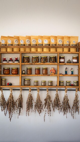 A wooden shelf with various jars of preserved foods and herbs. 5