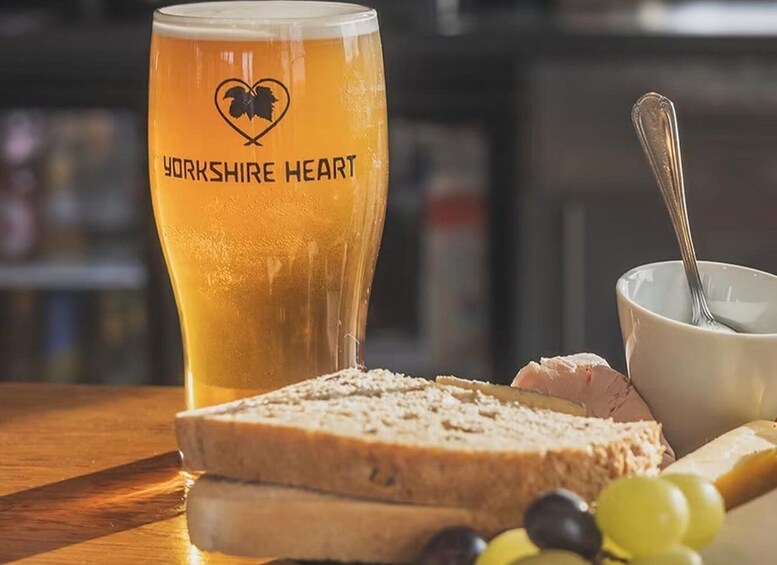 A glass of beer with Yorkshire Heart logo, a slice of bread, a bowl with a spoon, and some grapes. 4