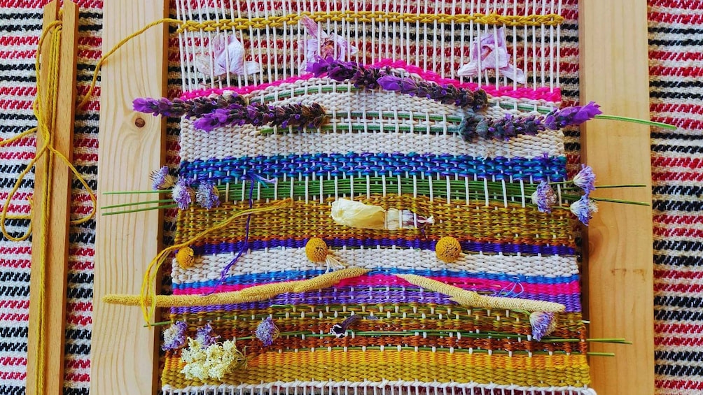 A colorful woven textile with various patterns and colors, displayed on a wooden frame. 5