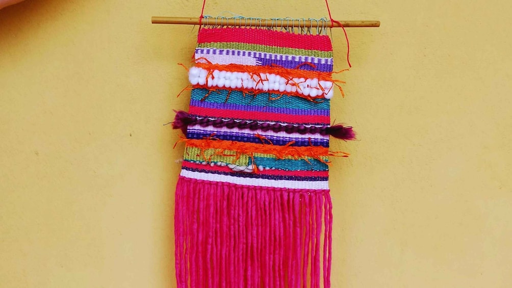 A colorful woven textile hanging on a wooden rod against a yellow wall. 2