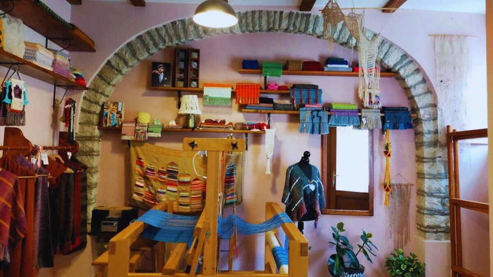 A weaving workshop with a loom, shelves of textiles, and a rustic stone archway. 1