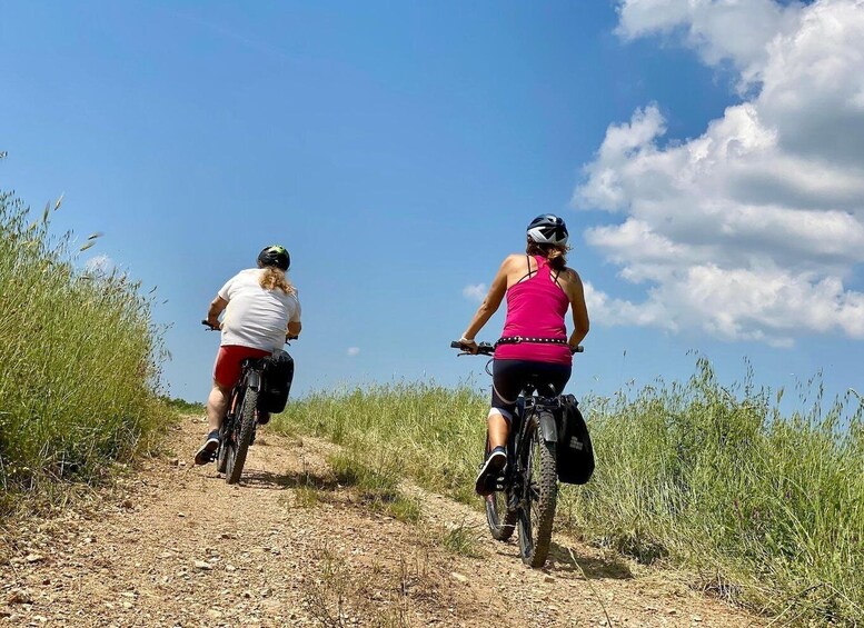 Two people riding bicycles on a dirt path surrounded by tall grass. 2
