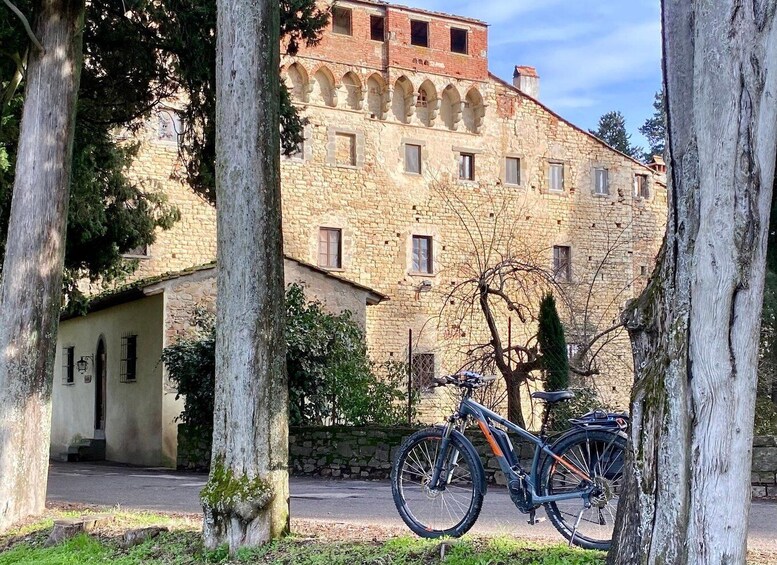 A stone building with arched windows, a bicycle, and trees. 1