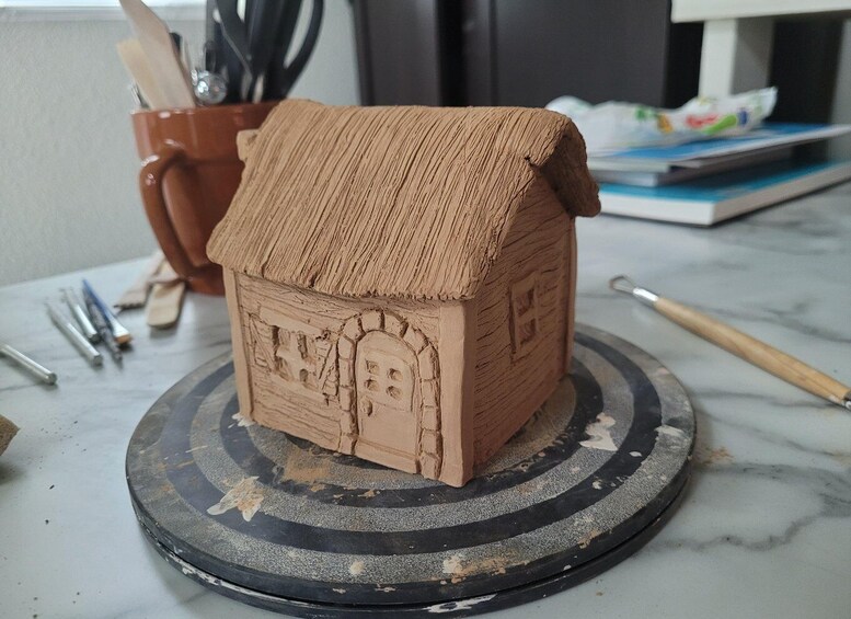 A clay model of a house with a pitched roof and a chimney, placed on a rotating stand. 4