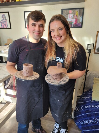 Two people holding pottery wheels with clay sculptures. 3