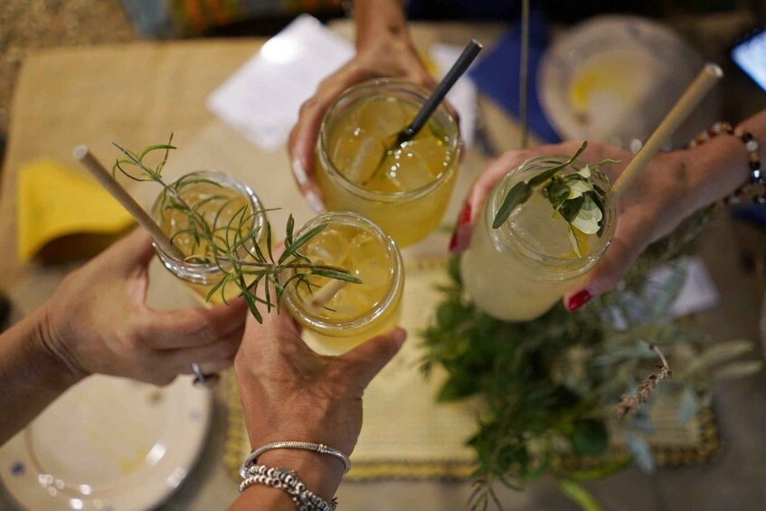 A group of people holding glasses with a yellow beverage, garnished with herbs. 2