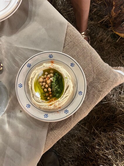 A plate of hummus with chickpeas and olive oil, placed on a table with a burlap cloth. 3
