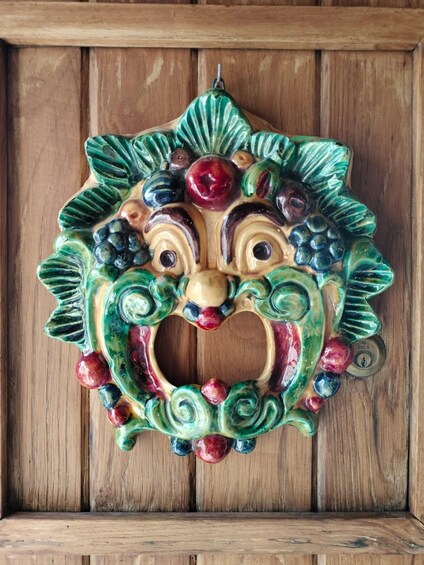 A colorful ceramic mask with a floral design, hanging on a wooden surface. 4