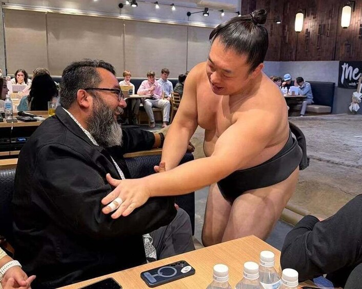 A sumo wrestler interacting with a seated man in a restaurant setting. 3