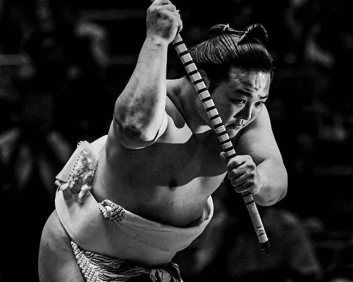 A person in a sumo wrestling outfit holding a bamboo straw. 2