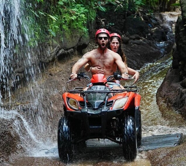 A person driving an ATV through a water stream in a forested area. 1