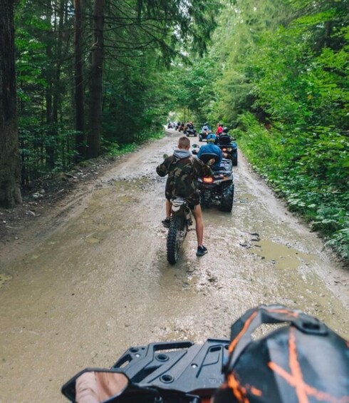 A muddy forest path with motorbikes and a person on a dirt bike. 3
