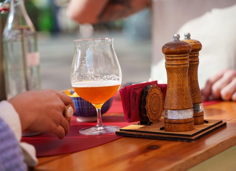 A glass of amber-colored beer on a wooden table with a red napkin and two wooden salt and pepper shakers. 3