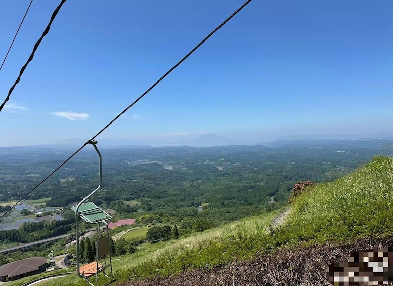A cable car moving over a landscape with a clear sky, green hills, and a distant view of a valley. 5