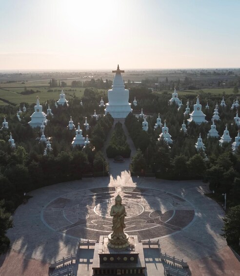 A large white stupa surrounded by smaller white stupas in a circular pattern, with a central statue in the foreground. 1