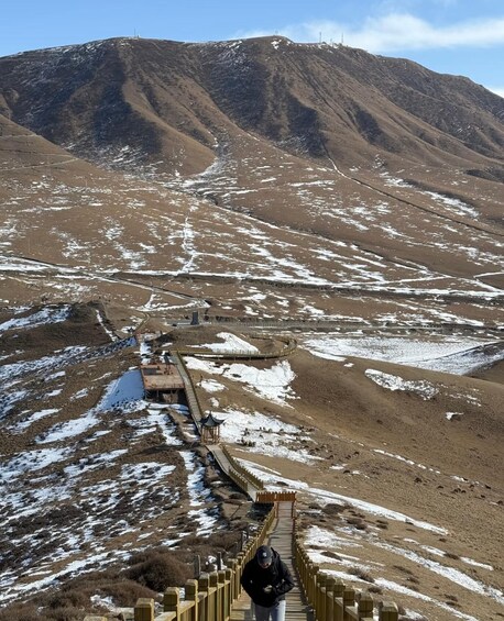 A person walking on a wooden boardwalk through a snowy landscape with a mountain in the background. 3