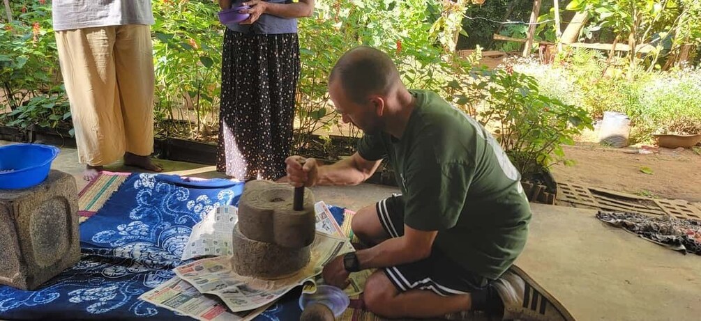 A person pounding a large stone with a wooden mallet. 1