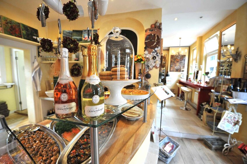 A bar with various bottles of Schlumberger wine, a glass display case with pastries, and a coffee machine. 1