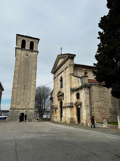 A historic stone tower with a clock and a church with a bell tower. 3