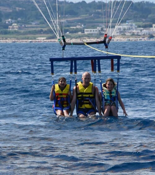 Three people on a parasail over water with a coastline in the background. 2