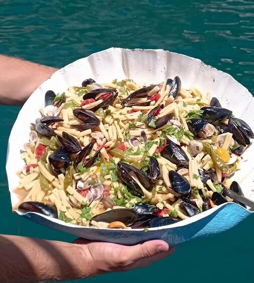 A person holding a shell-shaped dish filled with mussels, pasta, and vegetables. 3