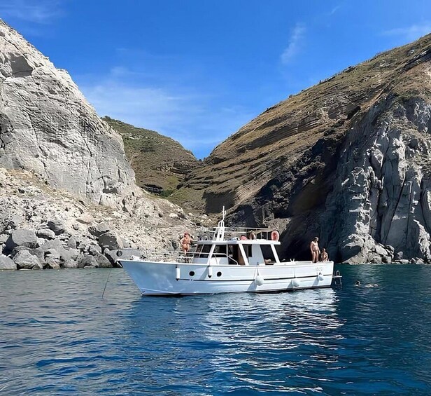 A boat anchored near rocky cliffs with clear blue water. 1