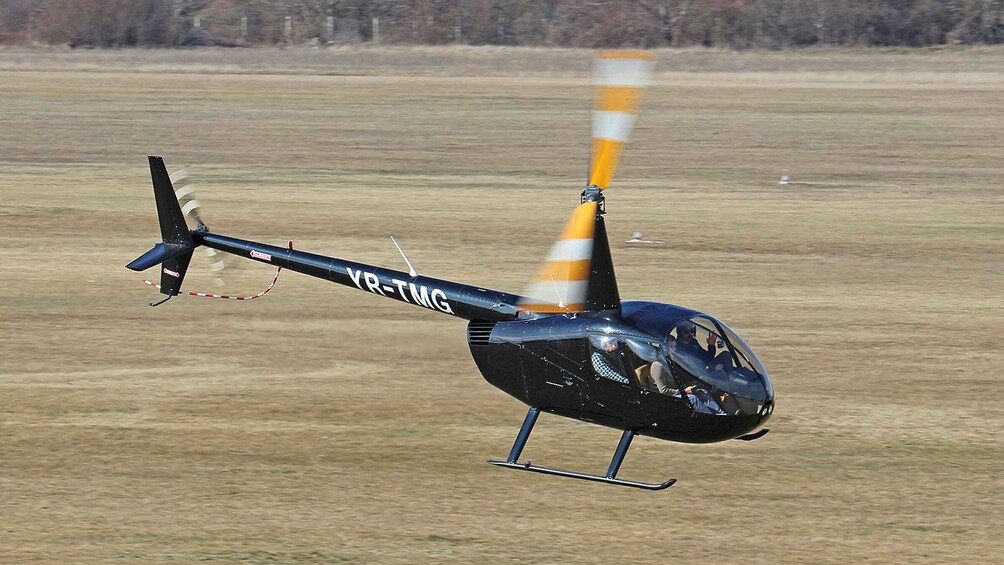 A helicopter with the registration 'YR-TMG' flying over a flat landscape. 5