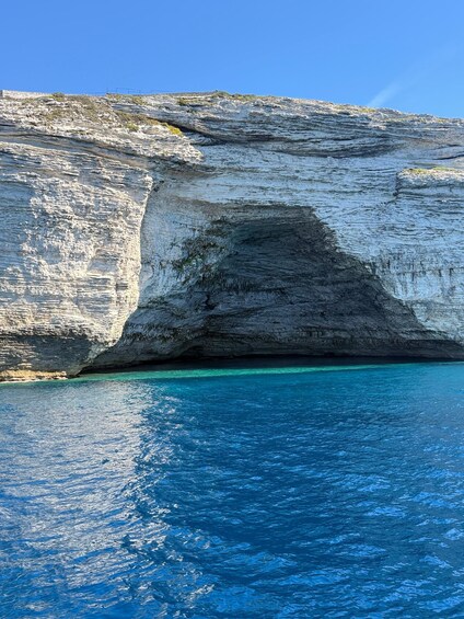 A coastal cliff with a cave entrance and clear blue water. 5