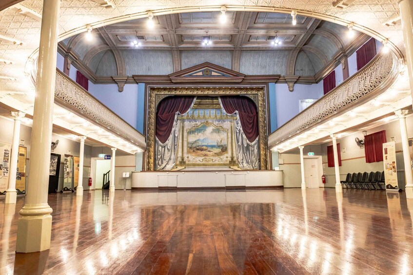 An ornate theater with a grand stage, high ceilings, and a polished wooden floor. 4
