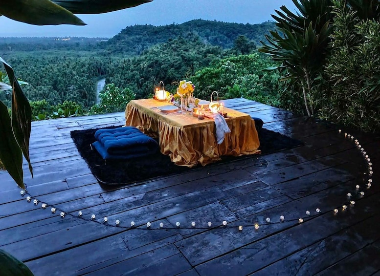 An outdoor dining setup with a table and chairs on a wooden deck, surrounded by lush greenery and a view of a forested landscape. 4