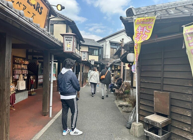A narrow street with traditional buildings, a shop with a sign reading 'YUFUIN BEARS,' and a banner advertising 'Dr. KissFish.' 2