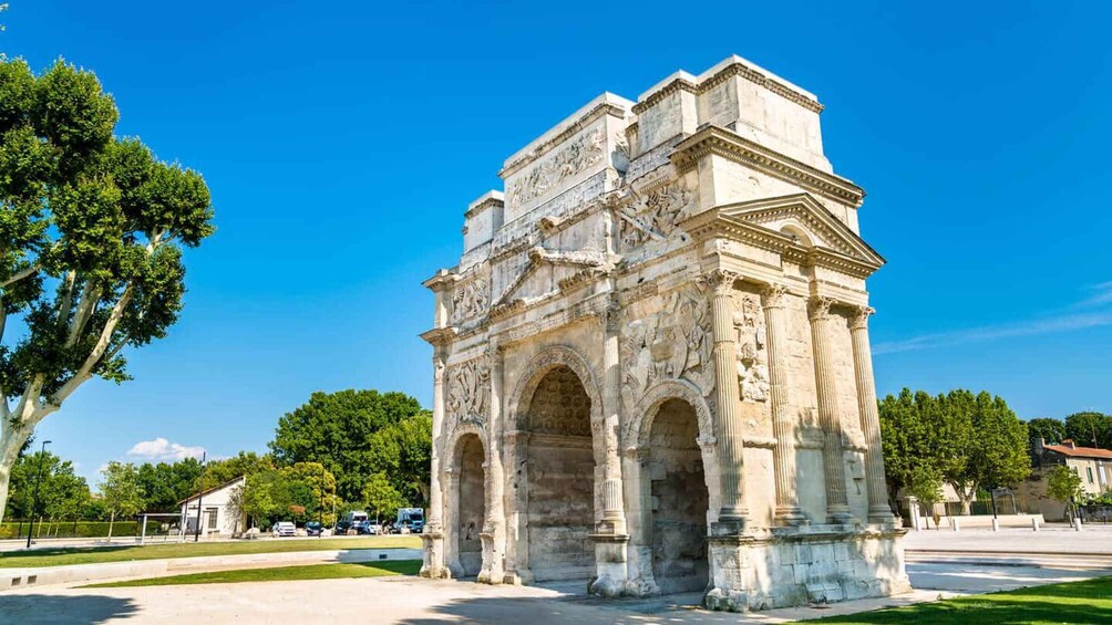 A historical monument with intricate carvings and columns, surrounded by trees and a clear sky. 1