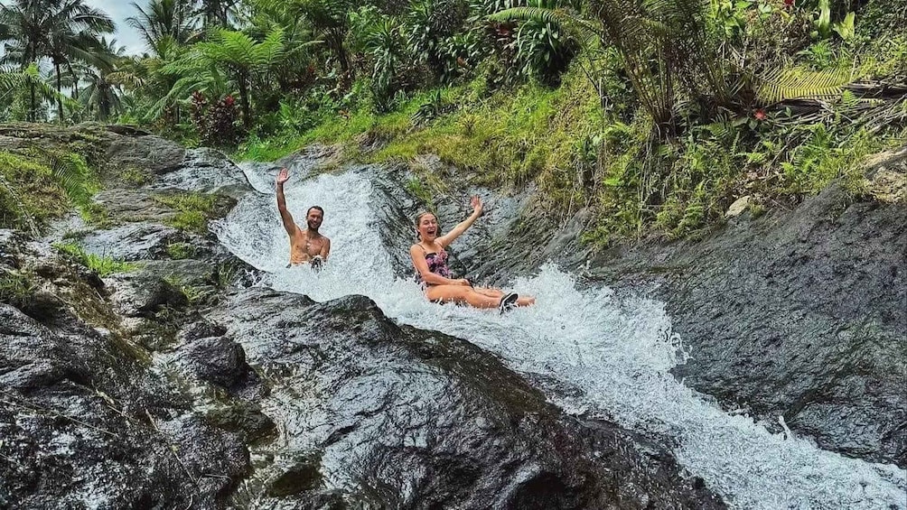 Two people sliding down a rocky waterfall in a tropical forest. 5