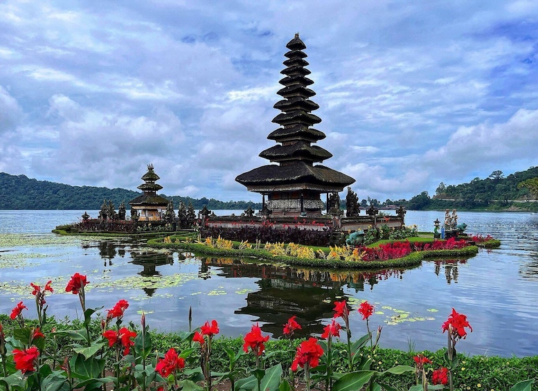A traditional Balinese temple with tiered roofs on a lake surrounded by lush greenery and red flowers. 3
