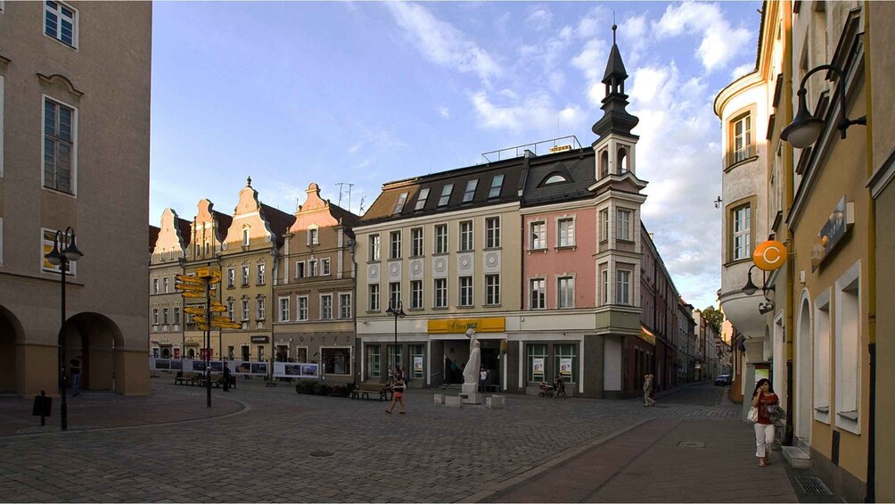 A cobblestone street lined with historic buildings, a statue, and a bank. 2