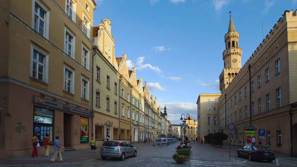 A cobblestone street lined with historic buildings, a prominent clock tower, and pedestrians. 3