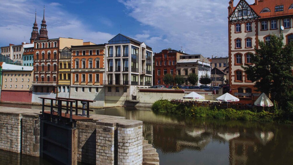 A riverside view with historic buildings, a modern glass structure, and a bridge. 5